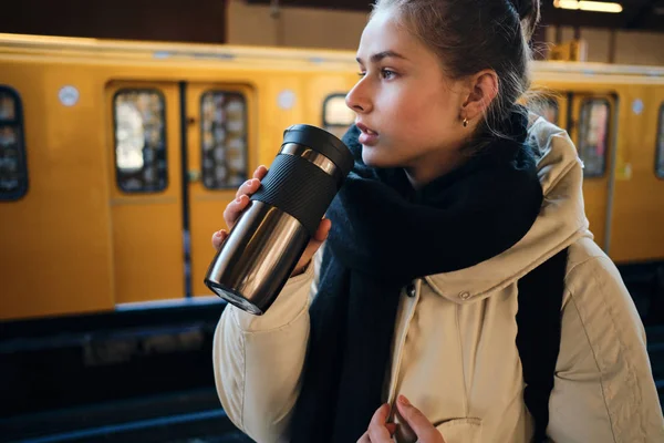 Seitenansicht eines zufälligen Touristenmädchens auf dem Bahnsteig, das wartende warme Getränke in der U-Bahn trinkt — Stockfoto