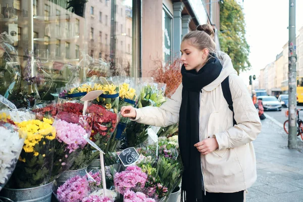 Atrakcyjny casual dziewczyna w dół kurtka starannie wybierając kwiaty na ulicy miasta — Zdjęcie stockowe