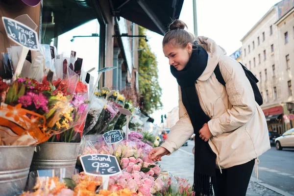 Gadis cantik yang santai dengan jaket senang hati memilih bunga indah di jalanan kota. — Stok Foto