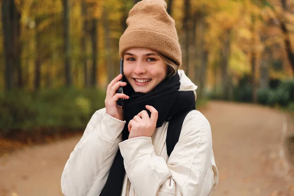 Красивая девушка говорит по сотовому телефону радостно глядя в камеру в красивом осеннем парке — стоковое фото
