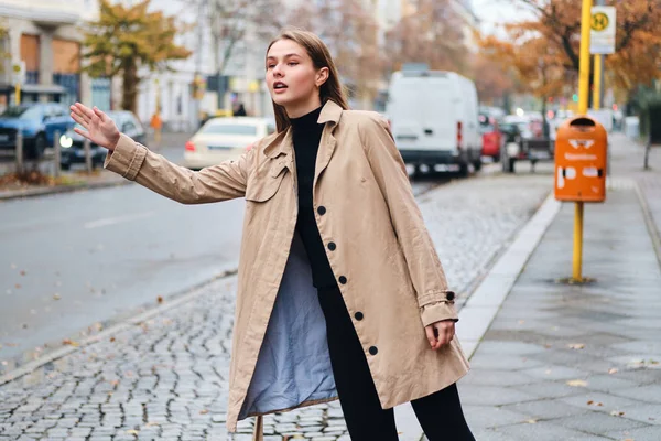 Piękna stylowa dziewczyna w płaszczu troskliwie łapie taksówkę na ulicy miasta — Zdjęcie stockowe