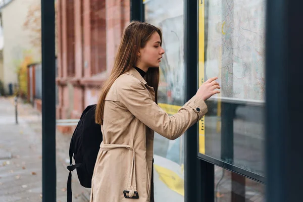 Attraktives Mädchen mit Rucksack nachdenklich aussehender Stadtplan an Bushaltestelle im Freien — Stockfoto