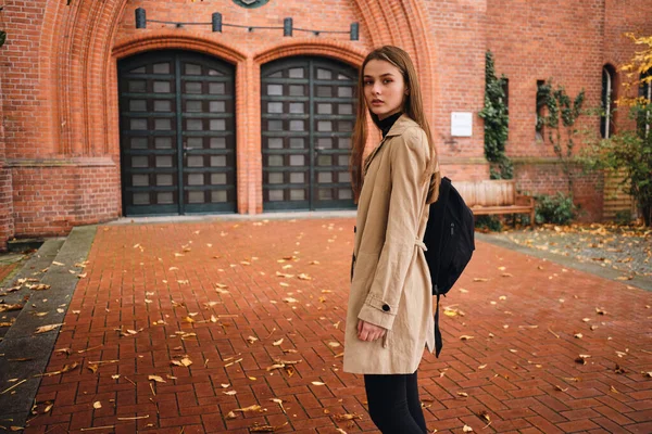 Привлекательная случайная девушка с рюкзаком пристально смотрит в камеру, гуляя по городской улице в одиночестве — стоковое фото
