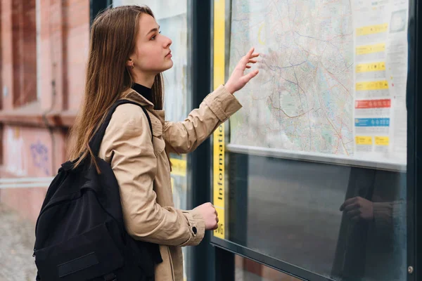 Houkutteleva rento tyttö reppu näköinen kaupungin kartta bussipysäkillä ulkona — kuvapankkivalokuva