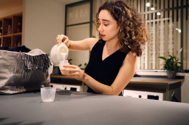 Güzel kız deterjan şişesini incelikle kullanıp çamaşırları yıkadı.