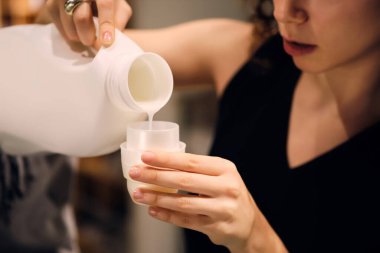 Kapalı kapılar ardında elinde deterjan şişesiyle çamaşır yıkayan bir kız.