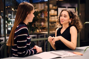 İki güzel kız mutlu bir şekilde konuşarak modern self-servis çamaşırhanesinde birlikte yıkanmayı bekliyor.