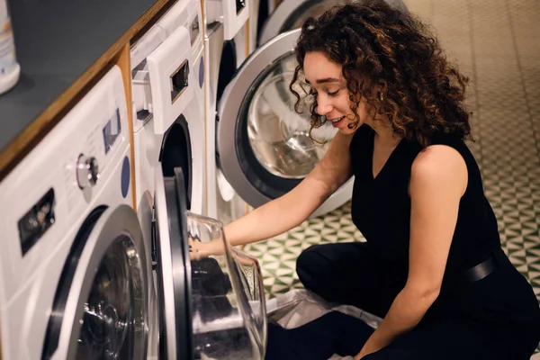 Bella ragazza sognante caricare i vestiti in lavatrice nella moderna lavanderia self-service — Foto Stock