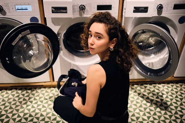 Привлекательная брюнетка стирает одежду в современной прачечной самообслуживания — стоковое фото