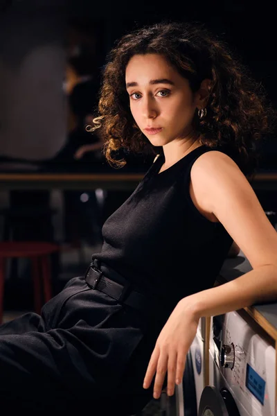 Menina elegante bonita olhando atentamente na câmera esperando lavagem na lavanderia self-service à noite — Fotografia de Stock