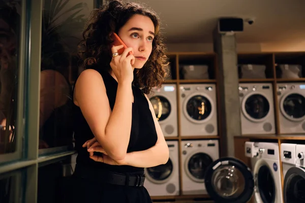 Bella ragazza che parla su smartphone in attesa di lavaggio in lavanderia self-service di notte — Foto Stock
