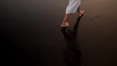 Genç bir kadının tropikal adada siyah kumsalda yürürken yakın plan fotoğrafı.