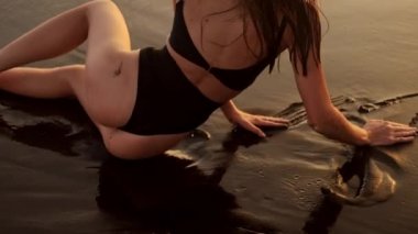 Güzel, ince bir kızın, tropikal bir adada, siyah kumsalda dinlenmesinin arka görüntüsü.