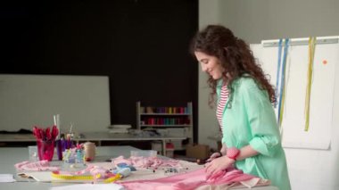 Genç ve güzel terzi, rahat terzi stüdyosunda dokularla mutlu bir şekilde çalışıyor.