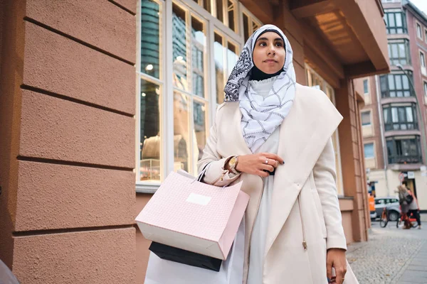 Young beautiful Arabic woman in hijab walking around city street after shopping