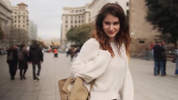 在美丽的城市广场上 跟踪着一个背着背包快乐地摆着相机的迷人而快乐的女孩的照片 — 图库视频影像