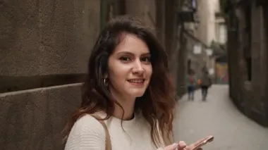 Akıllı telefonlu neşeli İspanyol kız kameraya bakıp dar sokaklara gülüyor.
