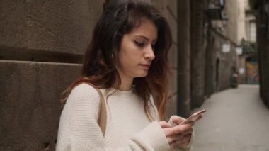 Güzel, sıradan İspanyol bir kız Barcelona dar caddesinde akıllı telefon kullanıyor.