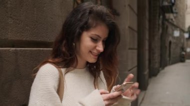 Güzel Türk gülümseyen kız Barselona dar caddesinde mutlu bir şekilde akıllı telefon kullanıyor.