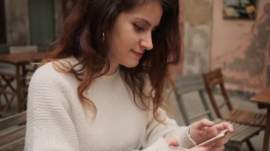 Çekici, gülümseyen İspanyol bir kızın açık kafede akıllı telefon kullanmasını yakından çek.