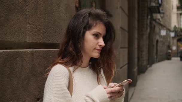 在巴塞罗那狭窄的城市街道上 一个迷人的 随意使用智能手机的女孩被跟踪镜头 — 图库视频影像
