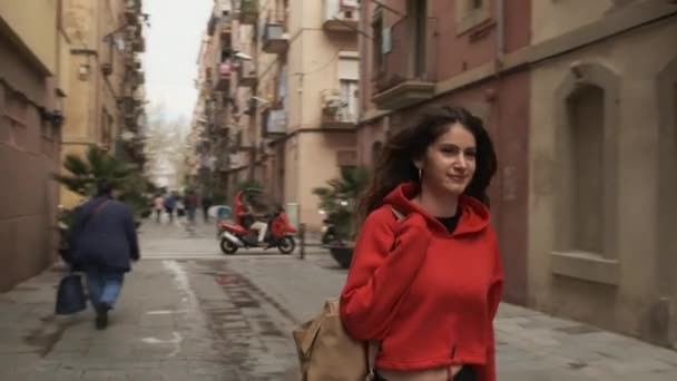 他的惊慌失措的黑发女郎背着背包快乐地沿着舒适的城市街道走着的跟踪镜头 — 图库视频影像