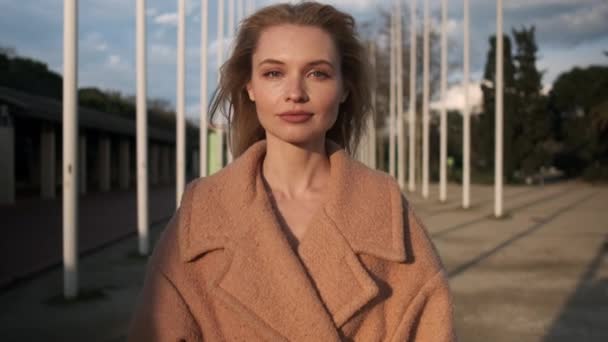 金发美女穿着外套 自信地看着街上的摄像机 日落时站在室外的模特 — 图库视频影像