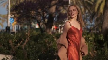 Paltolu ve ipek elbiseli romantik sarışının açık havada düşünceli yürüyüşünü çekiyoruz.