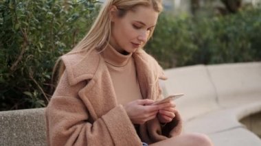 Şehir parkındaki bankta akıllı telefon kullanan çekici sarışın kızın portresi