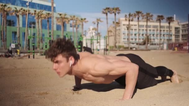 在海滩的功能性训练中追踪年轻肌肉男子推举的镜头 适合巴塞罗那海滨健身的人 — 图库视频影像