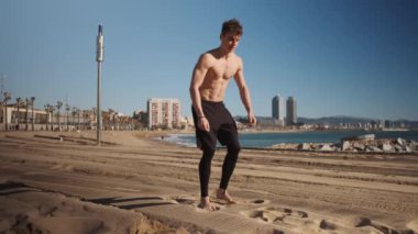 Genç kaslı adam Barcelona sahilinde deniz kenarında egzersiz yaparken akrobatik egzersiz yapıyor.