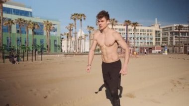 Genç kaslı adamın Barcelona 'daki şehir plajında takla atarken ya da yan takla atarken görüntüsü.