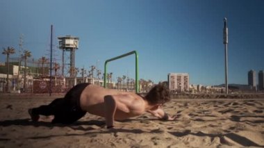 Genç yakışıklı kaslı adam Barcelona sahilinde egzersiz yapıyor.