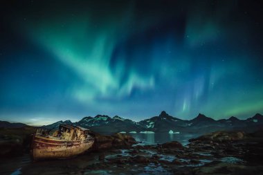 Aurora ön planda terk edilmiş balıkçı teknesi ile Grönland Dağları üzerinde