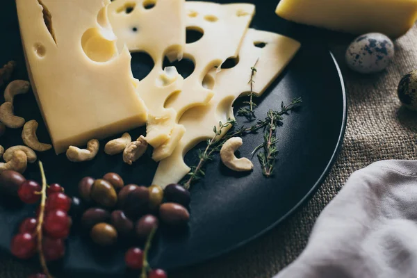 Meyveler, fındık ve kaju fıstığı ile süslenmiş şık siyah çanak üzerinde yalan delikli peynir. Yemek ve şarap içmek iyi bir şirket için aperatifler.