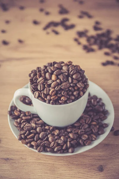 coffee cup filled by coffee beans on wooden background