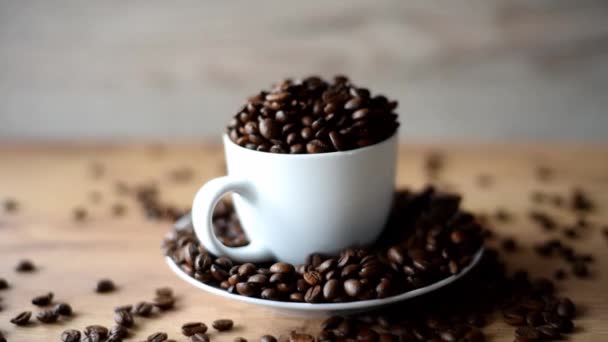 Кофейная чашка, наполненная кофейными зернами на деревянном фоне — стоковое видео