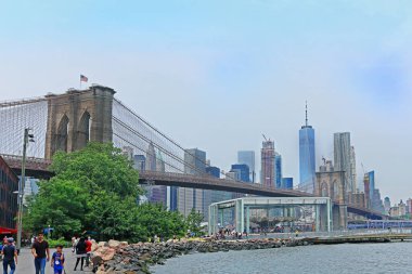 New York, ABD - 5 Haziran 2019: Brooklyn Köprü Parkı 'nda New York' taki East River 'ın yanında nehrin üzerindeki ünlü Brooklyn köprüsü ile yürüyen turist ve yerel halk.