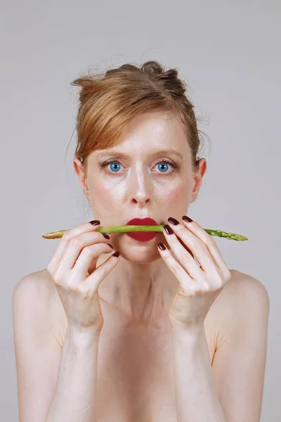 Młoda Kobieta Trzyma Surowe Szparagi Między Czerwonymi Ustami — Zdjęcie stockowe