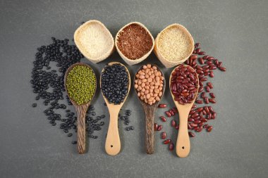 Hububat ve tohum fasulye (siyah fasulye, kırmızı fasulye, fıstık, Mung fasulye, Tayland Yasemin pirinç, kahverengi pirinç ve beyaz pirinç) gri arka plan üzerinde tahta kaşık sağlık için yararlı.