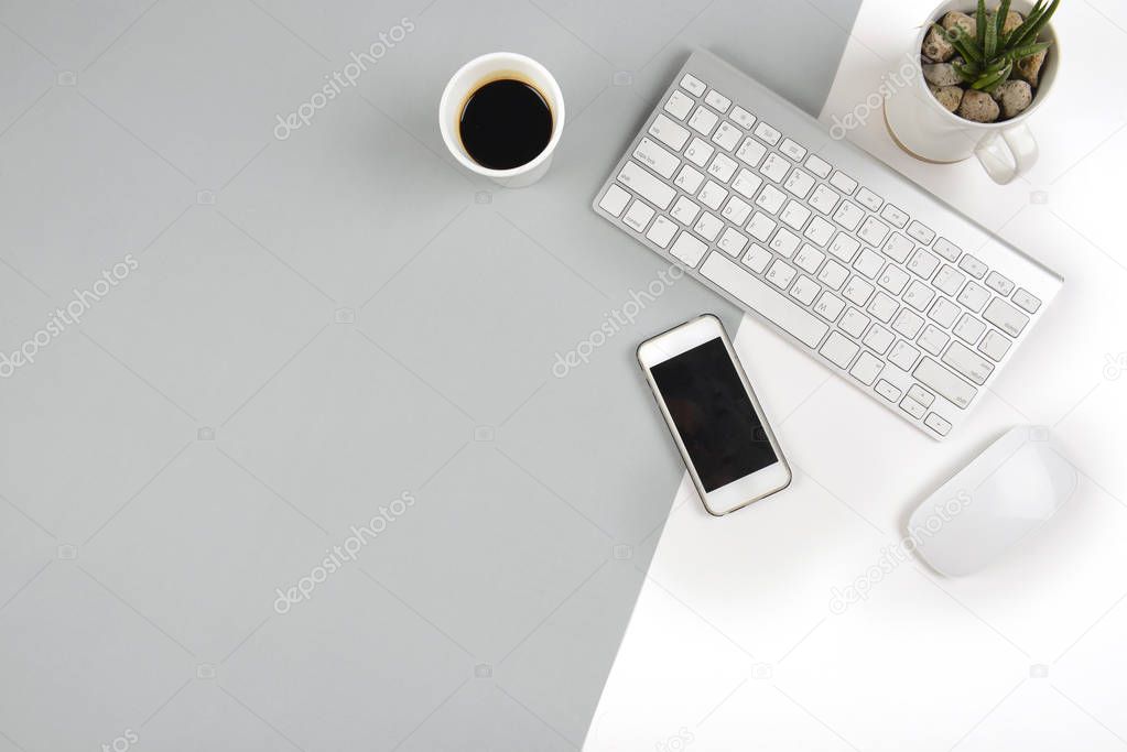 Office table with  keyboard, mouse, and smartphone on modern two tone (white and grey) background.