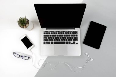 Dizüstü bilgisayar, dijital tablet ve modern iki ton (beyaz ve gri) arka plan üstünde hareket eden telefon ile ofis masaları.