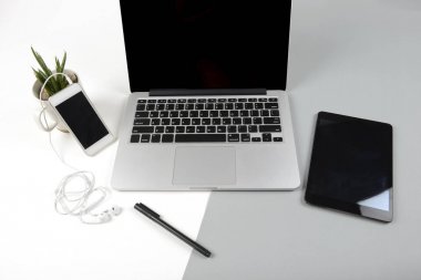 Dizüstü bilgisayar, dijital tablet ve modern iki ton (beyaz ve gri) arka plan üstünde hareket eden telefon ile ofis masaları.