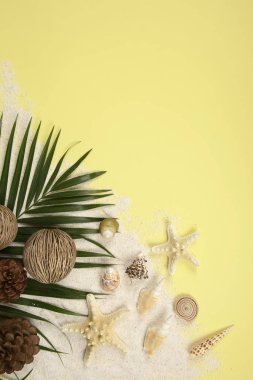 Yaz kavramı ve Sarı zemin üzerine kumlu plaj aksesuarları (kabukları, deniz yıldızı, Hindistan cevizi yaprağı).