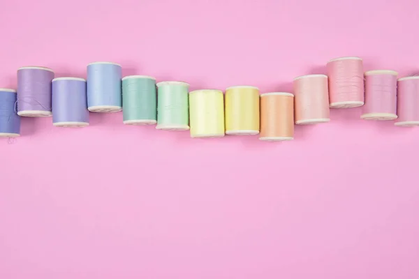 Flat lay of colored thread rolls for sewing on pink background,