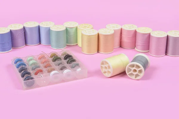 Flat lay of colored thread rolls for sewing on pink background,