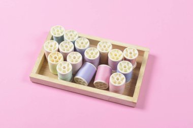 Düz lay renkli iplik dikiş için ahşap kutusunda pembe bir arka plan, dikiş ve iğne işi kavramı üzerinde rulo.