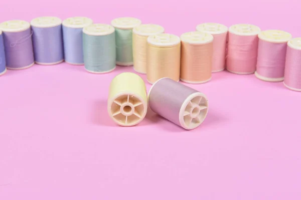 Flat lay of colored thread rolls for sewing on pink background, Sewing and needlework concept.