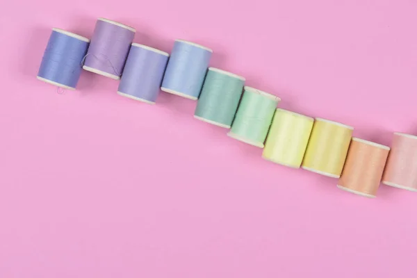 Flat lay of colored thread rolls for sewing on pink background,