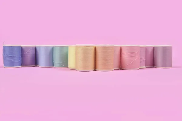 Flat lay of colored thread rolls for sewing on pink background,